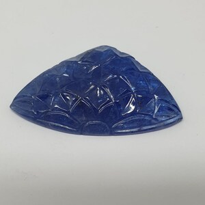May include: A carved blue gemstone with a fan-shaped design. The gemstone is a triangular shape with a smooth, polished surface.