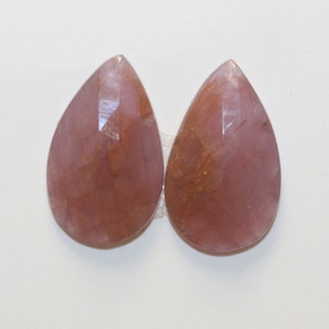 Peut inclure: Deux pierres précieuses roses en forme de larme avec une taille facetée. Les pierres précieuses ont une apparence translucide avec une légère teinte dorée.
