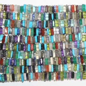 Puede incluir: Una hebra de cuentas de piedras preciosas de colores, cada cuenta tiene una forma rectangular y un color y un patrón diferentes. Las cuentas están hechas de varios tipos de piedras preciosas, incluyendo amatista, turquesa y jaspe.