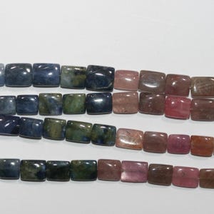 Op de afbeelding: Strengen vierkant geslepen edelsteen kralen in tinten blauw, groen, roze en bruin. De kralen zijn aan elkaar geregen en tonen een verscheidenheid aan kleuren en natuurlijke patronen. Ideaal voor het maken van sieraden.