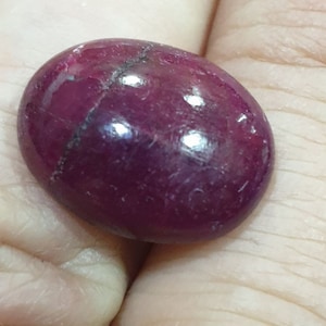 Könnte beinhalten: Ein ovaler, rotbrauner Cabochon-Edelstein mit einer glatten, polierten Oberfläche. Der Stein hat einen leichten Riss, der durch ihn verläuft.