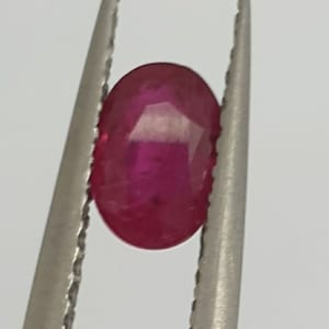 May include: A vibrant pink oval-shaped gemstone held in a pair of metal tweezers.