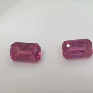 Pode incluir: Duas pedras preciosas retangulares e facetadas com um tom rosa profundo. As gemas têm um corte esmeralda clássico, mostrando sua estrutura interna e brilho. As pedras estão sobre um fundo branco.