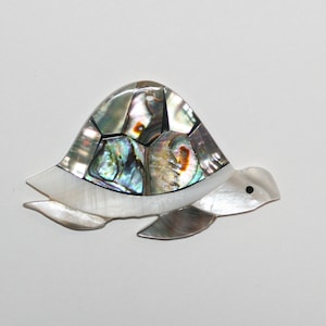 May include: A white and iridescent mother of pearl turtle ornament. The turtle's shell is made of many small pieces of iridescent shell, creating a mosaic effect. The turtle's head and legs are white.