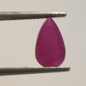 Peut inclure: Une pierre précieuse rose foncé en forme de larme, tenue par une pince.