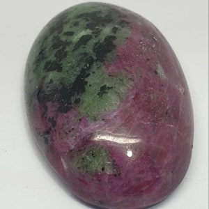 Puede incluir: Una piedra preciosa ovalada lisa de color verde y rosa con inclusiones negras. La piedra está pulida y tiene un acabado brillante.