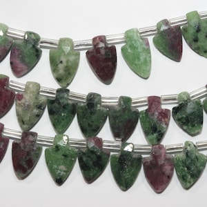 Puede incluir: Cadenas de cuentas de piedras preciosas en forma de escudo. Las cuentas son una mezcla de colores verde y burdeos, con un acabado pulido. Están ensartadas en un alambre plateado, perfectas para la creación de joyas.