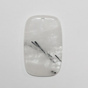 May include: White quartz pendant with black tourmaline inclusions. The pendant is rectangular with a hole at the top for hanging.