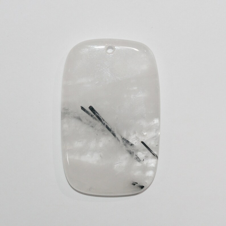 May include: White quartz pendant with black tourmaline inclusions. The pendant is rectangular with a hole at the top for hanging.