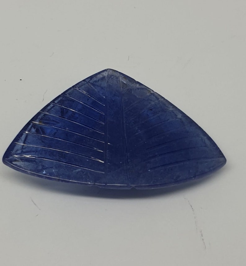 May include: A triangular blue gemstone with a carved leaf design.
