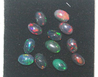 May include: A collection of oval-shaped black opals with vibrant flashes of color, including red, green, and blue. The opals are displayed on a black surface, showcasing their iridescent qualities. These gemstones are ideal for jewelry making.