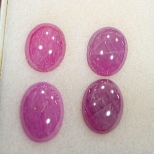 Op de afbeelding: Vier ovaalvormige, cabochon geslepen edelstenen met een levendige magenta-roze kleur. Elke steen heeft een glad, gepolijst oppervlak met zichtbare interne insluitingen en lichtreflecties, gerangschikt in een twee-bij-twee raster.