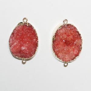 Könnte beinhalten: Zwei rosa Achat-Kristallscheiben mit goldfarbenen Metallakzenten. Jede Scheibe hat oben ein Loch zum Aufhängen.