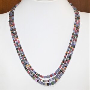 Puede incluir: Un collar de múltiples hilos hecho de pequeñas piedras preciosas facetadas en tonos azules, rosas y verdes. El collar está en capas y tiene un aspecto delicado y femenino.