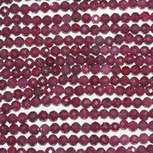 Puede incluir: Una hebra de cuentas de piedras preciosas facetadas de color rojo intenso. Las cuentas son redondas y tienen un acabado liso y pulido.