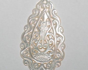 May include: A white mother of pearl pendant with an intricate, carved design. The pendant is shaped like a teardrop and features a floral motif.