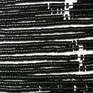 Könnte beinhalten: Eine Strähne schwarzer runder Perlen, jede Perle ist durch einen kleinen silbernen Abstandshalter getrennt. Die Perlen sind auf einem dünnen Draht aufgefädelt.