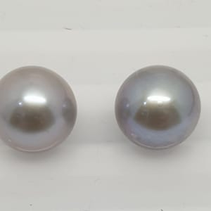 Könnte beinhalten: Zwei runde, irisierende graue Perlen. Die Perlen haben eine glatte, glänzende Oberfläche.