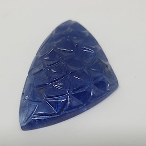 May include: A blue, triangular, carved gemstone with a geometric pattern.