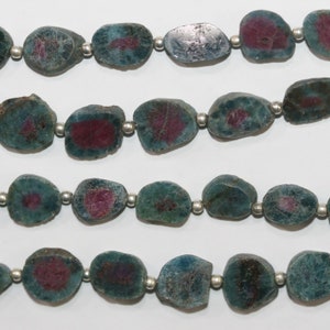 Puede incluir: Una hebra de cuentas de piedras preciosas verdes y rosas con separadores plateados. Las cuentas son de forma ovalada y tienen una textura rugosa y natural.