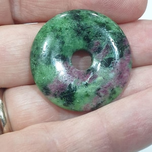 Può includere: Pietra verde e rosa a forma di ciambella con un foro al centro.