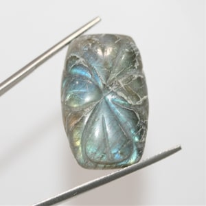 Può includere: Una pietra preziosa di labradorite scolpita con un bagliore iridescente blu-verde. La pietra preziosa è di forma ovale e ha una superficie liscia e lucida.