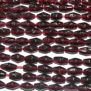 Peut inclure: Une collection de perles rouge foncé, translucides et en forme de losange, enfilées sur un fil rouge fin. Les perles présentent un design géométrique à facettes avec une finition polie, disposées en plusieurs rangées parallèles.