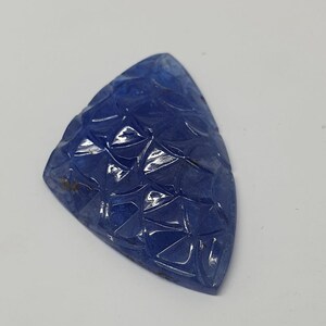 May include: A blue gemstone carved with a geometric pattern. The gemstone is triangular in shape and has a smooth, polished surface.