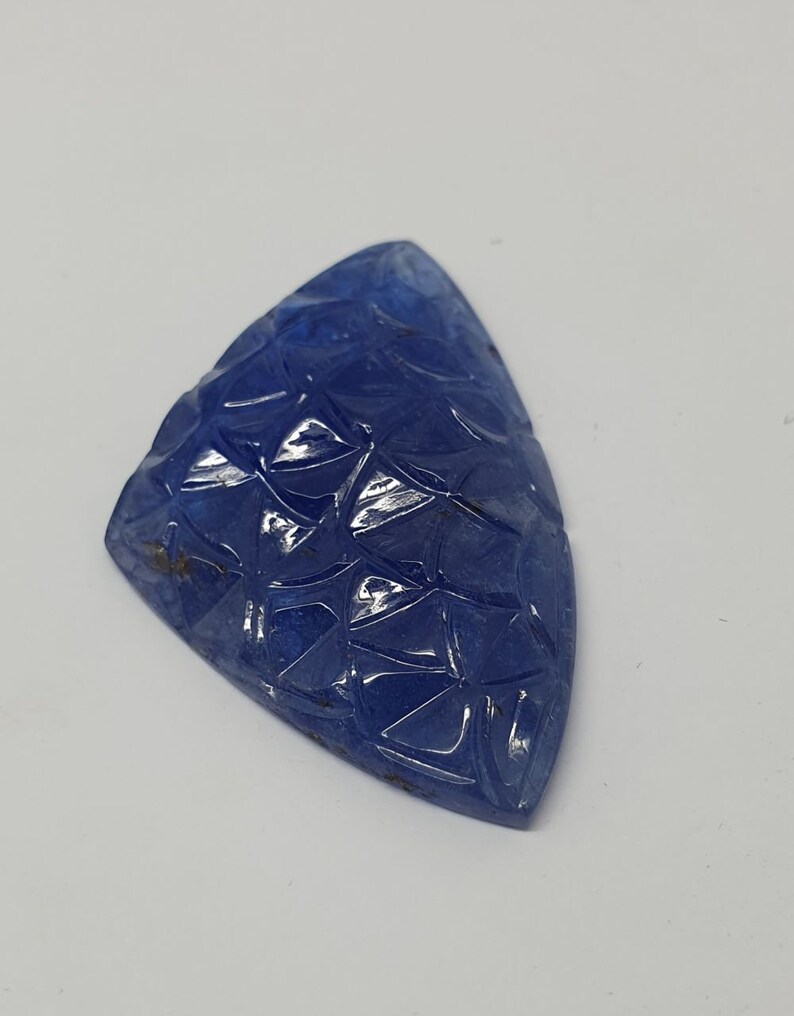 May include: A blue gemstone carved with a geometric pattern. The gemstone is triangular in shape and has a smooth, polished surface.