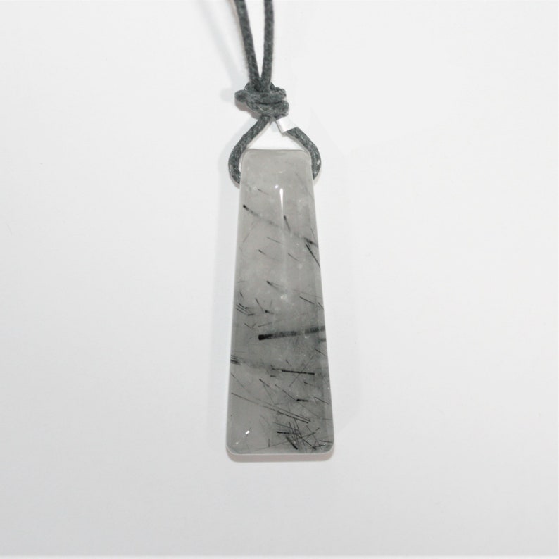 May include: A clear quartz pendant with black inclusions, hanging from a gray cord.
