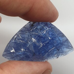 May include: A carved blue gemstone with a geometric pattern. The gemstone is shaped like a triangle with rounded edges.