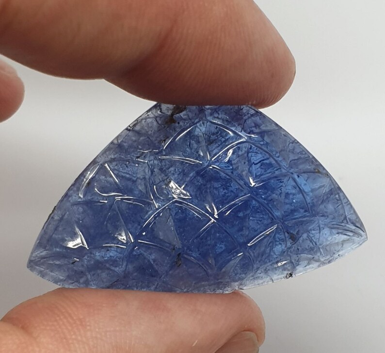 May include: A carved blue gemstone with a geometric pattern. The gemstone is shaped like a triangle with rounded edges.