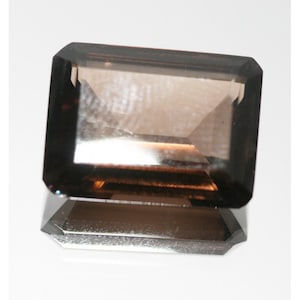 May include: A dark brown, faceted, rectangular gemstone with a smooth, polished surface.