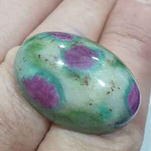 Könnte beinhalten: Ein ovaler Cabochon-Edelstein mit einem grün-rosa marmorierten Muster auf weißem Hintergrund.
