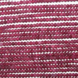 May include: A strand of deep pink faceted gemstone beads. The beads are small and round, and they are strung on a clear thread.