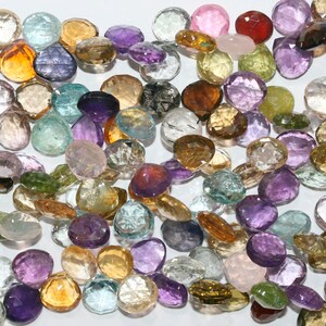 Puede incluir: Surtido de cuentas de piedras preciosas facetadas de colores en varios tonos de morado, verde, azul, marrón y rosa. Las cuentas son de forma ovalada y tienen un acabado liso y pulido.