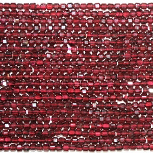 Può includere: Una collana di perline di pietra preziosa sfaccettata rosso scuro. Le perline sono piccole e di forma quadrata, con una finitura lucida.