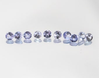 May include: A row of nine round, faceted, light purple gemstones on a white background.