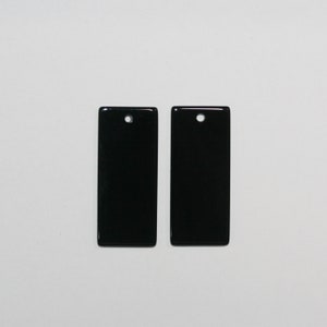 Puede incluir: Dos colgantes rectangulares negros con un acabado brillante. Cada colgante tiene un pequeño agujero en la parte superior para ensartar. Los colgantes se muestran sobre un fondo blanco.
