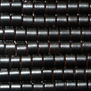 Peut inclure: Gros plan sur un groupe de perles cylindriques noires. Les perles ont une finition lisse et brillante et sont disposées en grille.