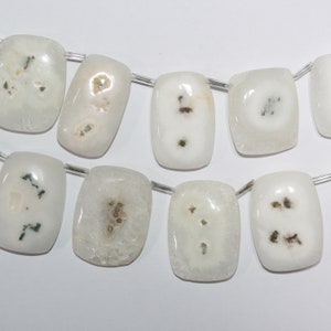 May include: Strand of white and cream-colored gemstone beads. Each rectangular bead features unique patterns of brown and green inclusions. The beads are strung on a thin, clear wire, ideal for jewelry making.