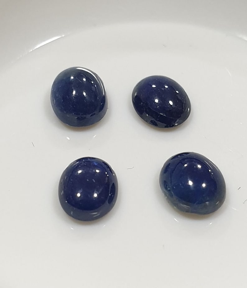 May include: Four oval-shaped, dark blue gemstones on a white surface.