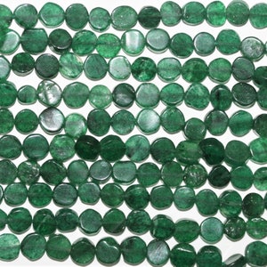 Può includere: Una collana di perle di giada verde. Le perle sono rotonde e piatte, con una forma leggermente irregolare. Hanno una finitura liscia e lucida.