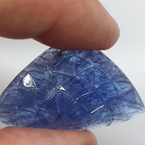 May include: A carved blue gemstone with a geometric pattern. The gemstone is shaped like a triangle and has a smooth, polished surface.