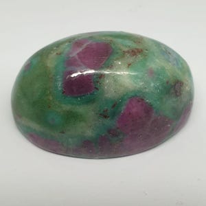 Pode incluir: Uma gema oval cabochão com uma superfície polida. A pedra tem um padrão de redemoinho de verde, rosa e branco.