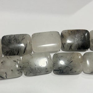 Può includere: Una collana di perle rettangolari in quarzo bianco traslucido con inclusiones nere. Le perle sono lisce e lucidate.