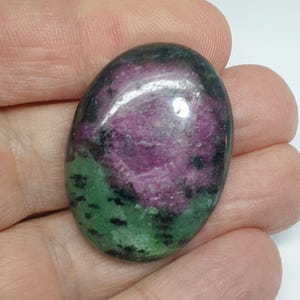 Könnte beinhalten: Ovaler grüner und rosafarbener Edelstein-Cabochon mit schwarzen Flecken.