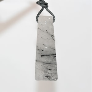 May include: A clear quartz pendant with black tourmaline inclusions, hanging from a black cord.