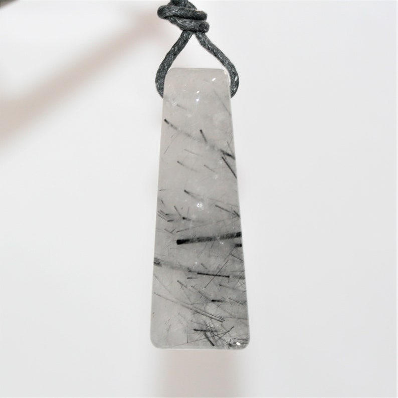 May include: A clear quartz pendant with black tourmaline inclusions, hanging from a black cord.