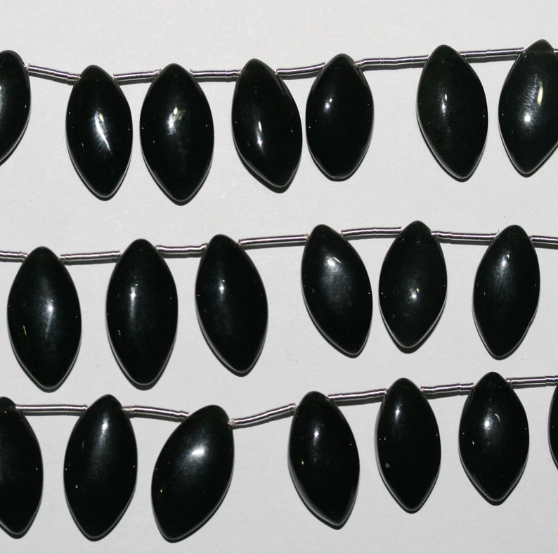Peut inclure: Un fil de perles de pierres pr&eacute;cieuses noires, chaque perle est en forme de larme avec une finition lisse et polie. Les perles sont enfil&eacute;es sur un fil d'argent.